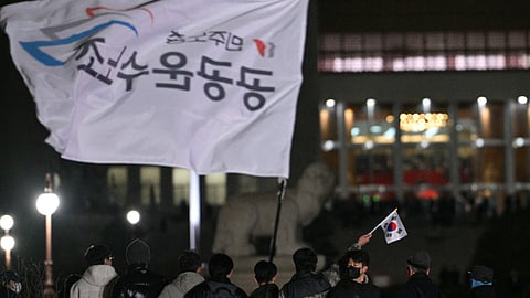 A man holds a South Korea flag as he gathers with others outside the National Assembly in Seoul on 4 December 2024, after South Korea President Yoon Suk Yeol declared martial law. South Korea's President Yoon Suk Yeol on 3 December declared martial law, accusing the opposition of being "anti-state forces" and saying he was acting to protect the country from "threats" posed by the North.