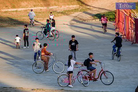 Children and teenagers ride rented bicycles in an open lot after school, enjoying the afternoon sun.