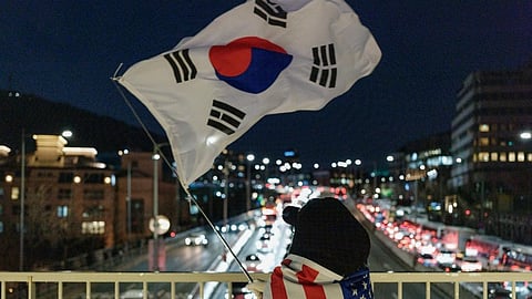 A supporter of impeached South Korean President Yoon Suk Yeol waves a South Korean flag as she wears a US flag on a pedestrian bridge near the President's residence in Seoul on January 9, 2025.