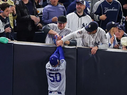 Fans Austin Capobianco (L) and John Peter (R) interfere with Mookie Betts #50 of the Los Angeles Dodgers as he attempts to catch a fly ball in foul territory during the first inning of Game Four of the 2024 World Series.