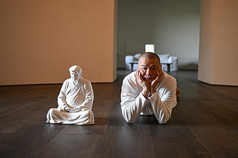 This photo taken on December 9, 2024 shows artist Hong Jinshi posing for photos next to a sculpture of US president-elect Donald Trump in a pose evoking the Buddha at his workshop in Xiamen, in southeastern China's Fujian province. Donald Trump is not typically known for his calm or reserve, but in a craftsman's workshop in rural China, the US president-elect sits in divine contemplation.