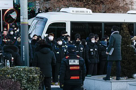 Police officers secure the path as a white vehicle leaves the residence of impeached South Korean President Yoon Suk Yeol in Seoul, early on 15 January 2025. South Korean investigators tried to arrest impeached President Yoon Suk Yeol on 15 January over his failed martial law bid, using ladders to enter his residence compound after clashes broke out when his guards blocked the main gate.