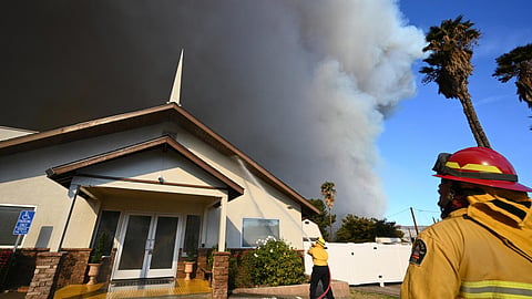 Private firefighters protect a church as the plume of smoke from the Hughes fire darkens the sky in Castaic, a northwestern part of Los Angeles, California, on January 22, 2025