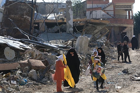 People carrying Hezbollah flags walk amid the rubble of buildings hit by Israeli bombing in the southern Lebanese border town of Aitaroun, as inhabitants return following the pullout of Israeli troops and the deployment of the Lebanese army, on 2 February 2025.