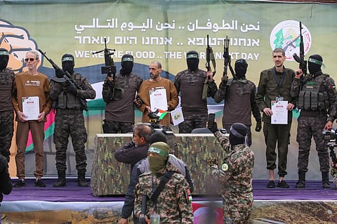 Palestinian Hamas fighters escort Israeli hostages (L-R, holding certificates) Ohad Ben Ami, Or Levy and Eli Sharabi on a stage before handing them over to a Red Cross team in Deir el-Balah, central Gaza, on February 8, 2025. Hamas militants handed over three Israeli hostages on February 8, as part of the fifth exchange under a fragile Gaza ceasefire, with 183 prisoners held by Israel due to be released later in the day.