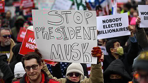 People hold up signs as they protest against US President Donald Trump and Elon Musk's "Department of Government Efficiency" (DOGE) outside of the US Department of Labor near the US Capitol in Washington, DC. Elon Musk has begun swinging his wrecking ball at the US government, with concerns growing over the unprecedented power that President Donald Trump has handed to the world's richest man.