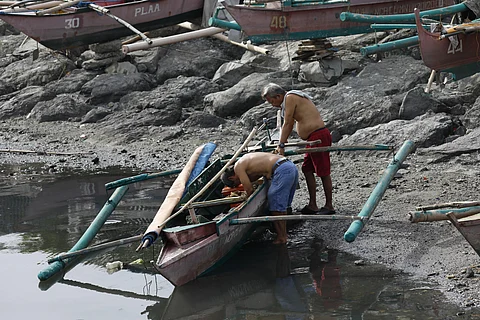 Fisherfolk repair their boat along the shores of Manila Bay, preparing for their next journey at sea. A Supreme Court ruling that allows commercial fishing in municipal waters is impacting the livelihood of fishermen nationwide.
