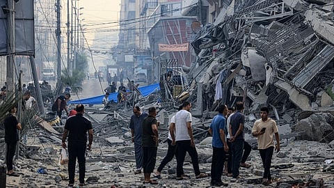 Residents walk along a debris-strewn street in front of a building that collapse during an Israeli air strike in Gaza City early on 8 October 2023. Photo by MAHMUD HAMS / AFP.