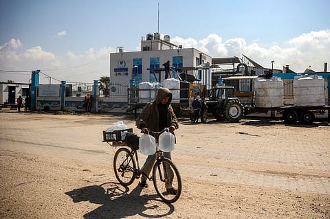 A youth pushes a bicycle loaded with filled-up water containers outside the Southern Gaza Desalination plant, which stopped working after Israel cut off electricity to the Gaza Strip, in Deir el-Balah in the center of the Palestinian territory on March 10, 2025.