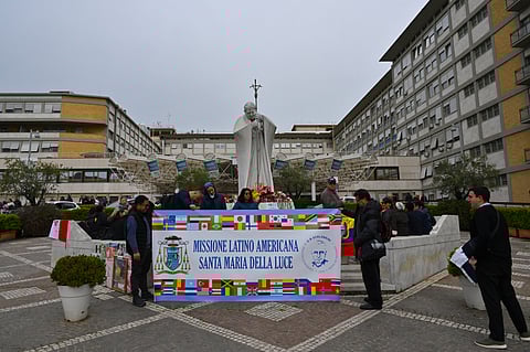 Faithfuls, priests and nuns hold a banner which reads, "Latin American Mission, Holy Mary of the Light", as they pray at the statue of John Paul II outside the Gemelli University Hospital where Pope Francis is hospitalised in Rome on 15 March 2025. Pope Francis marked a month in hospital on 14 March 2025, with football players sending him messages of support for his recovery from pneumonia, including the captain of his favorite team, San Lorenzo.