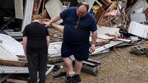 Justin Stievenart, right, uses his son, Jayson, 11, for balance while switching shoes outside of his destroyed home in Harmony Hills trailer park on 15 March 2025 in Poplar Bluff, Missouri.
