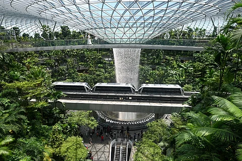 A WOMAN (top) walks across the bridge next to the Rain Vortex, the world's tallest indoor waterfall, and a mono-rail train going through the Jewel Complex at Singapore Changi Airport in Singapore on 10 April 2025.