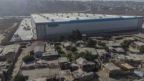 An Amazon fulfillment center looms over informal housing in Tijuana, Mexico. The warehouse services customers in Tijuana and nearby markets including Mexicali, Tecate, Ensenada, and Rosarito—underscoring the stark contrasts along the supply chain reshaped by shifting U.S. trade policies.