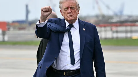 Donald Trump raises his fist while walking on a tarmac, wearing a navy suit and tie with a stern expression on his face.