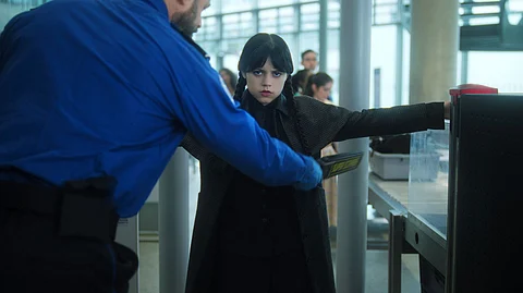 Wednesday Addams is frisked by security at an airport in a scene from season 2 of 'Wednesday.'