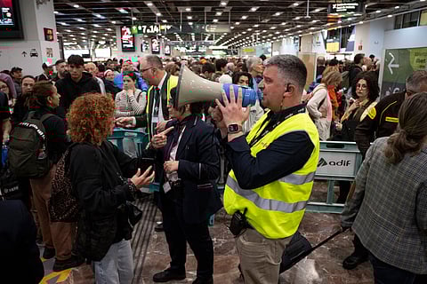 An employee of Spanish state-owned rail company RENFE speaks into a megaphone to share information as passengers wait before boarding their train at Sants railway station in Barcelona on 29 April 2025, a day after a massive power cut affecting the entire Iberian peninsula and the south of France.