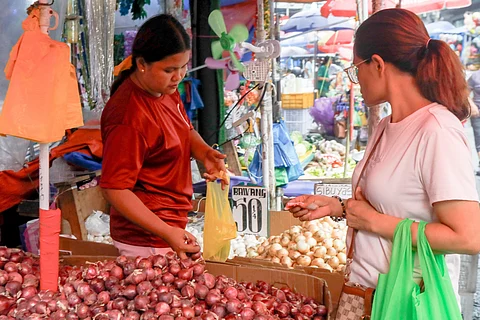 An onion vendor sells her merchandise to a market goer at a sidewalk stall along Divisoria in Manila on Friday.