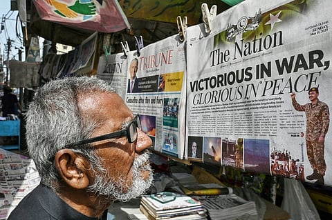 A resident reads a morning English newspaper at a roadside stall in Karachi on May 11, 2025, showing headline related to ceasefire agreement between India and Pakistan. India and Pakistan traded accusations of ceasefire violations early on May 11, hours after US President Donald Trump announced that the nuclear-armed neighbours had stepped back from the brink of full-blown war.