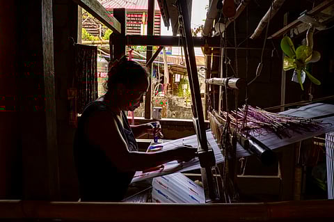 An Inabel weaver works on a handloom inside a traditional workshop in Ilocos Norte, weaving red and blue silhouettes into fabric that forms the official logo of Palarong Pambansa 2025.