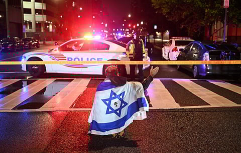 A man draped in the Israeli flag, bearing a cross and the name "Jesus" at its center, gestures as Metropolitan Police officers secure the area outside the Capital Jewish Museum following a shooting that left two people dead in Washington, DC, in the early hours of May 22, 2025. Two Israeli embassy staffers were shot dead late Wednesday, May 21, outside a Jewish museum in Washington by a gunman who shouted "free Palestine," authorities said, with US officials and Israeli diplomats expressing shock and outrage over the killings.