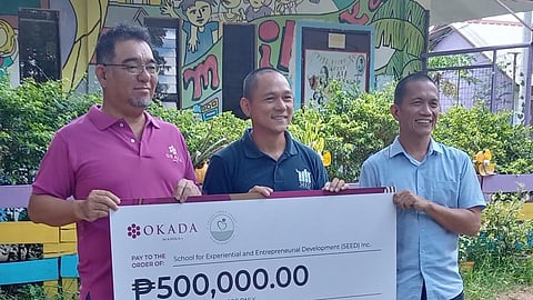 SUGIYAMA (left) presents Okada Manila’s symbolic cash donation to Bercasio (right) and Cruz. The money funded the agricultural training of nine SEED scholars.