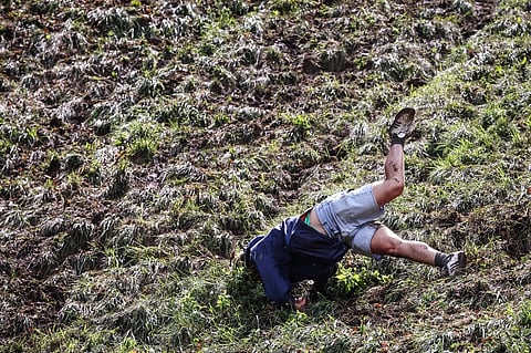 A competitor comes tumbling down the hill in pursuit of a round Double Gloucester cheese during the annual Cooper's Hill cheese rolling competition near the village of Brockworth, Gloucester, in western England, on 27 May 2024. The annual Cooper's Hill Cheese Rolling involves competitors chasing an eight pound Double Gloucester cheese down a steep hill.