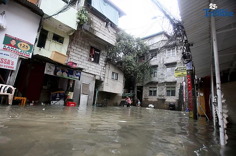 RESIDENTS clear trash from knee-deep floodwaters outside their home in Roxas District, Quezon City, on Saturday, July 19, 2025, after continuous rains brought by the Habagat intensified by Severe Tropical Storm Crising. Red Cross personnel monitor the area.