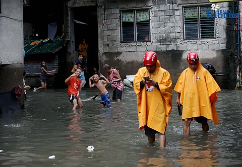 Residents clear trash from knee-deep floodwaters outside their home in Roxas District, Quezon City, on Saturday, July 19, 2025, after continuous rains brought by the Habagat intensified by Severe Tropical Storm Crising. Red Cross personnel monitor the area.