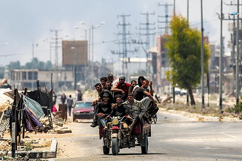 Men ride together in the back of a tricycle cart along Salaheddin road in Deir el-Balah in the central Gaza Strip while behind smoke billows from Israeli bombardment.