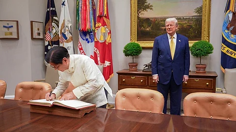 President Ferdinand Marcos Jr. logs at the White House while US President Donald Trump watches him.