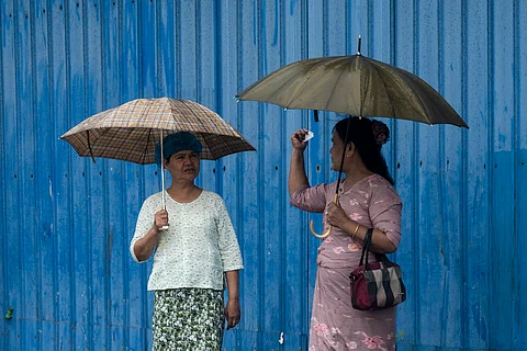 Women use umbrellas to cover from the rain as they wait for the bus in Yangon on July 21, 2025.