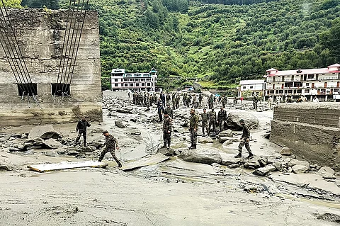 this handout photograph released on August 6, 2025 by the Indian Army shows security and relief personnel building a crossing across a stream of dense sludge during a search and rescue operation, a day after a cloudburst caused a massive mudslide and flash floods in India's Uttarakhand state. The Indian army brought in sniffer dogs, drones and heavy earth-moving equipment to search for scores of people missing after the deadly Himalayan flash floods. At least four people were killed and more than 50 are unaccounted for after a wall of muddy water and debris tore down a narrow mountain valley, smashing into the town of Dharali in Uttarakhand state, rescue officials said on August 6.