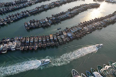 This photo shows an aerial view of two boats sailing past fishing boats moored in anticipation of Typhoon Podul, at the Gaoqi Mintai Centre Fishery Port in Xiamen, China's southeastern Fujian province on August 12, 2025. Typhoon Podul pounded Taiwan on August 13, shutting down businesses in the south, grounding hundreds of flights and knocking out power for tens of thousands of households.
