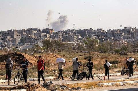 A smoke cloud erupts in the background from an explosion as people walk with bags of humanitarian aid they received at a distribution centre run by the US and Israeli-backed Gaza Humanitarian Foundation (GHF), as they cross the so-called "Netzarim corridor" in the central Gaza Strip, on August 22, 2025. The United Nations officially declared a famine in Gaza on August 22, the first time it has done so in the Middle East, with experts warning 500,000 people face "catastrophic" hunger. UN agencies have long been warning of the deteriorating humanitarian situation in Gaza, particularly as Israel steps up its offensive against Hamas.