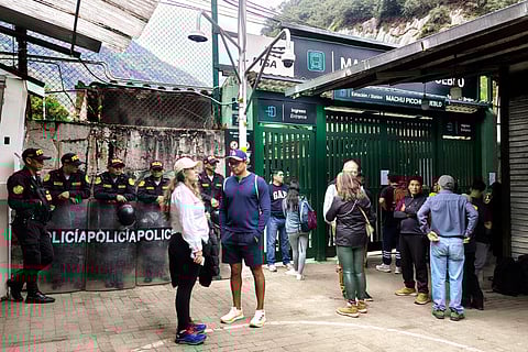 Police officers stand guard next to a group of tourists at the train station in Machu Picchu Pueblo, Cusco department, Peru, on September 16, 2025. Peru evacuated some 1,400 tourists overnight from the train station that serves the Inca citadel of Machu Picchu, while about 900 others remained stranded as protesters blocked the railway tracks to demand a new company be chosen to run the buses that ferry visitors from the Aguas Calientes train station, at the foot of Machu Picchu, to the site itself.