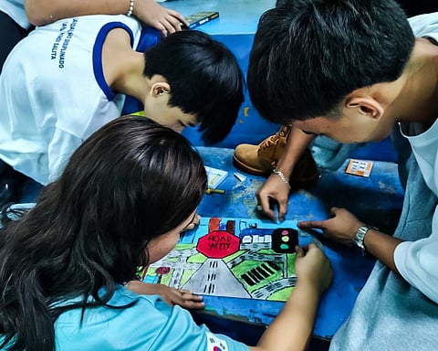 STUDENTS work together on a road safety poster highlighting traffic signs and safe driving reminders.