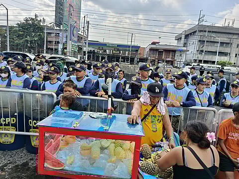 Police Officers in People Power Monument are on Standby while "Trillion Peso March" is ongoing. A Vendor peacefully go to his day-to-day life selling pineapple and other fruits.