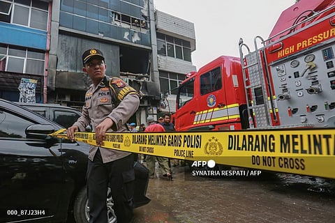 A member of the Indonesian police sets up a barricade tape to cordon off a seven-storey building where firefighters extinguished a fire that killed at least 20 people in central Jakarta on December 9, 2025.