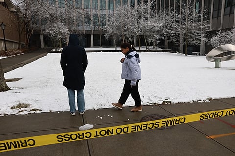 People pause outside of the engineering and physics building at Brown University, the site of a mass shooting yesterday that left at least two people dead and nine others injured, on December 14, 2025 in Providence, Rhode Island. A suspect in the shooting was detained overnight at a hotel in a nearby community following a manhunt across the prestigious university and the greater Providence area. The shooting took place around 4 p.m. on Saturday as students were preparing for exams and the holiday break.