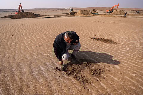 An Iraqi engineer examines the soil as excavators clear sand dunes and extract clay in the desert south of Samawah on December 21, 2025.
A new project to combat desertification has been launched, focusing on treating sand dunes before planting, in an effort to curb one of the country’s most destructive climatic phenomena. The initiative is being implemented across three southern governorates that are major sources of dust storms, and represents the first intervention of its kind by a non-governmental organization in these areas in years. It is funded by the Kuwait Fund for Arab Economic Development.