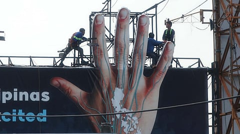 WORKERS fasten a giant hand to the skyline as politics looms large below, an image echoing Sen. Panfilo Lacson’s stance against officials turning public works into personal billboards.