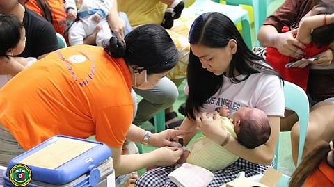 A MOTHER holds her son while being immunized against vaccine-preventable diseases during the launch of a free vaccination drive at the Caloocan Sports Complex in Caloocan City.