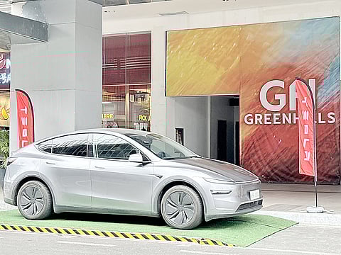 GRAY Tesla Model Y stands at the Greenhills entrance as visitors check out the electric lineup.