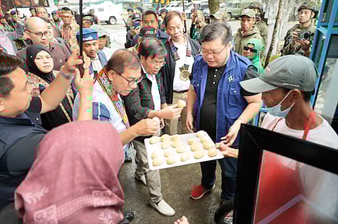 DOST Secretary Renato U. Solidum Jr. (on left with lay) and MILF chairperson of Camp Bushra JTFCT Jannati Mimbatas try the pandesal baked by former combatants from the bakery given by the DoST and OPAPRU.