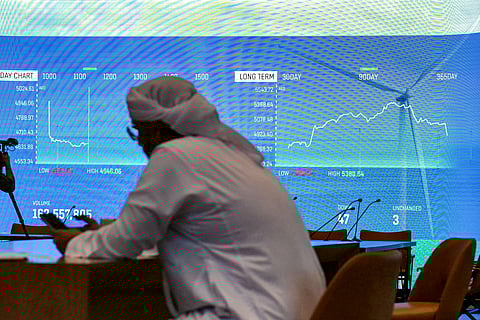A man browses his phone while sitting near a screen displaying the stock indices at the Dubai Financial Market (DFM) stock exchange in Dubai on 7 April 2025.