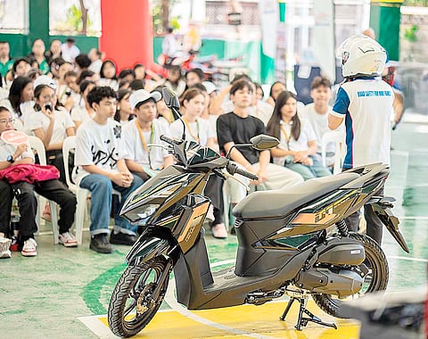 DEMONSTRATION shows proper riding practices as students watch a road safety lesson with a motorcycle display.