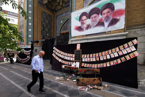 A man walks past images of Iran's late supreme leaders Ayatollah Ruhollah Khomeini (above L) and Ayatollah Ali Khamenei (Above C) next to newly elected supreme leader Mojtaba Khamenei (above R), and photos strung along the wall of children killed on the first day of the war in an alleged US-Israeli missile strike on a school in the southern Iranian city of Minab, outside a mosque in the capital Tehran on 25 April 2026. On 28 February, Israel and the United States launched strikes on Iran, killing its supreme leader and triggering a war that spread across the Middle East.