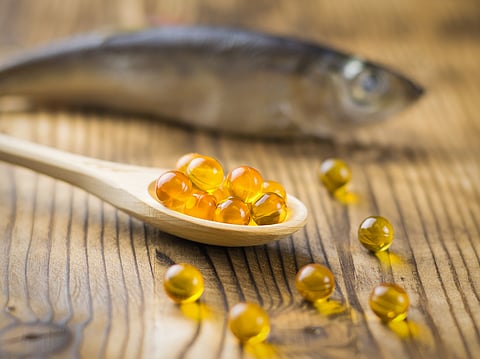 Bright wooden spoon with capsules of fish oil on the background of the fish. 