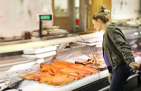 Woman shopping fresh salmon in supermarket retail store.