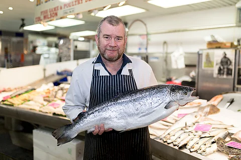 Fishmonger holding a salmon on a market in England, UK.